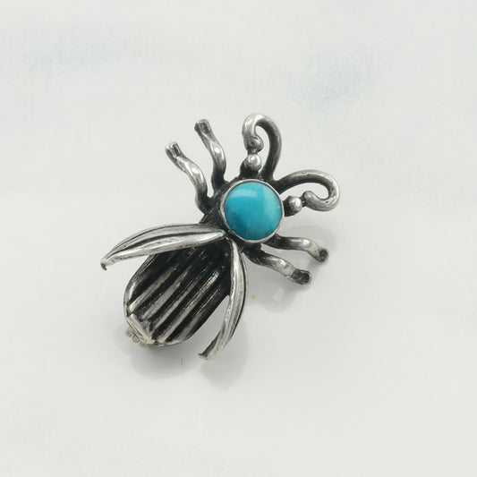 Silver spider-shaped earring with turquoise stone on a light gray background