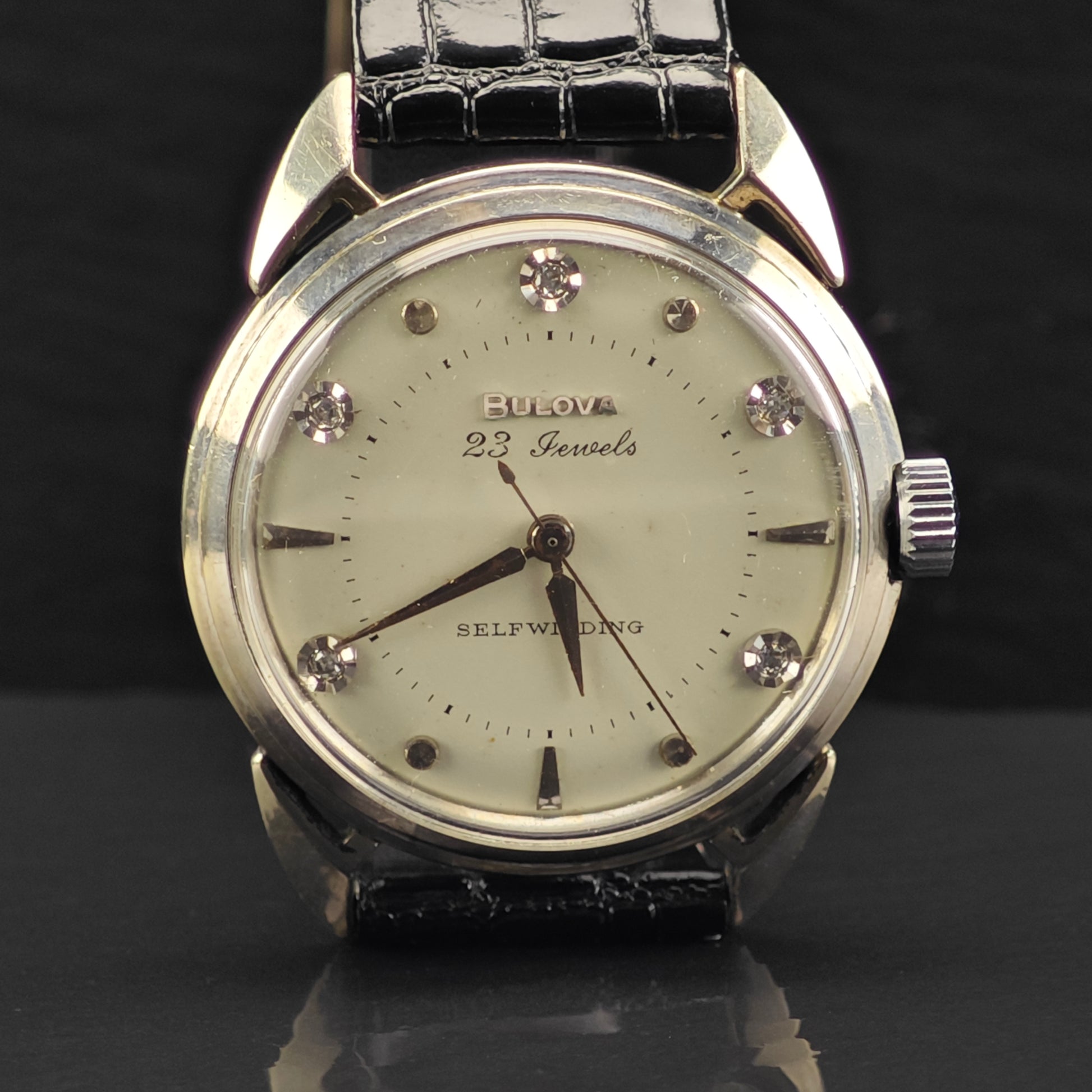 Vintage Bulova watch with a black leather strap and diamond-studded face on a dark background