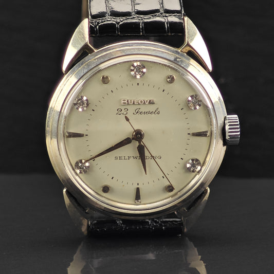Vintage Bulova watch with a black leather strap and diamond-studded face on a dark background