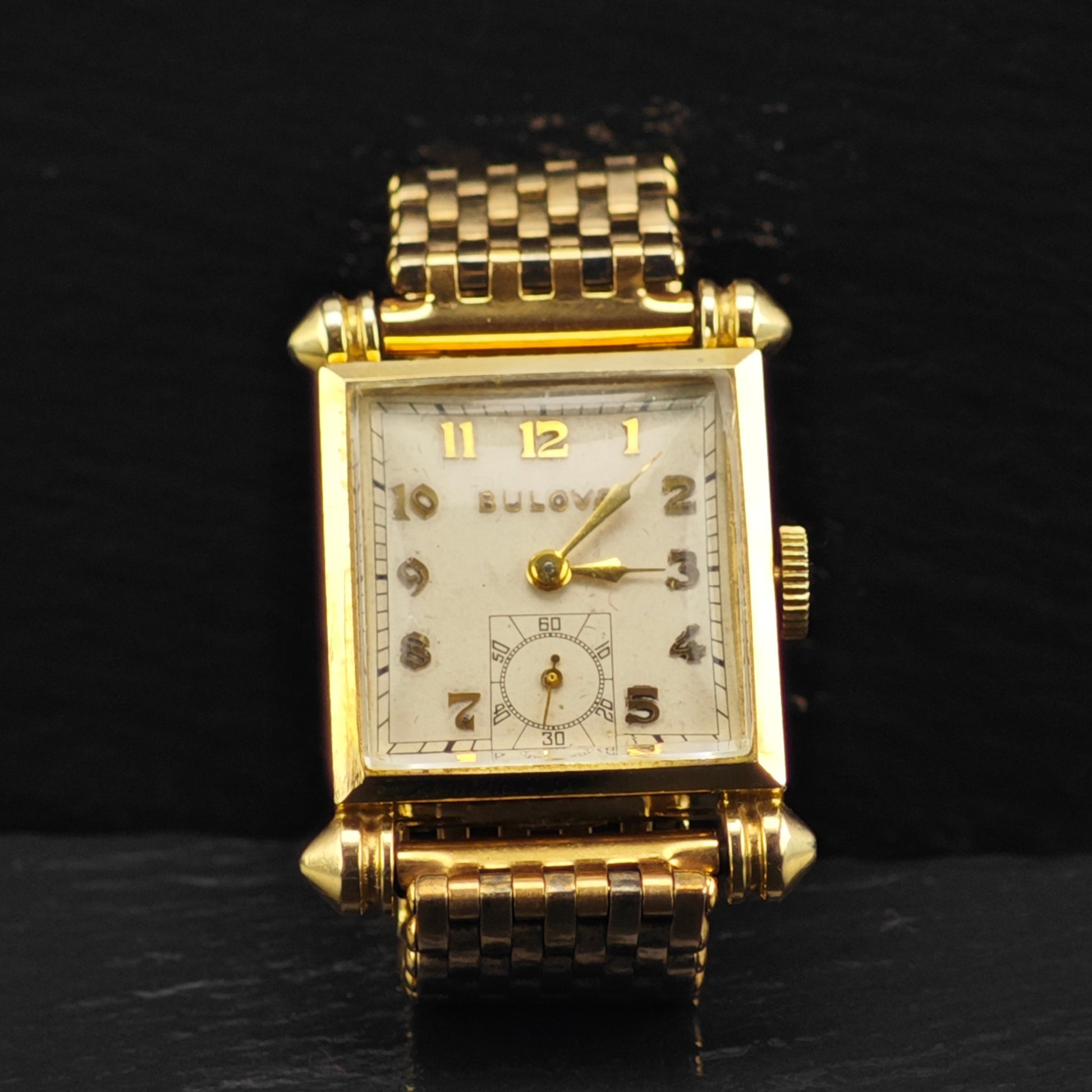 Gold wristwatch with a checkered band on a black background